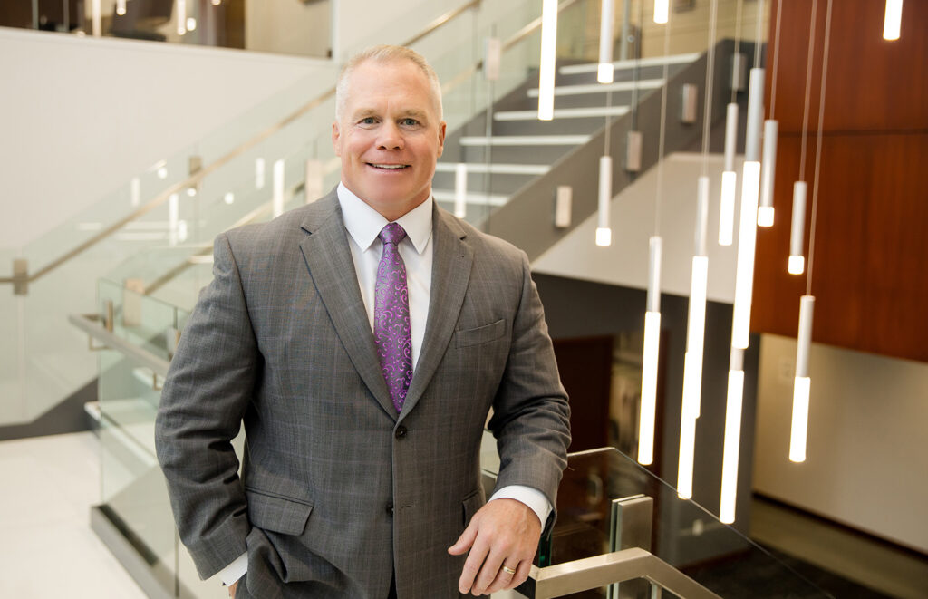 Curt Heidman smiles while standing in front of a staircase